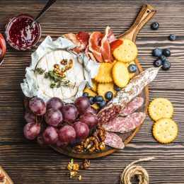Red wine, wooden boards, cold meat, variety of cheese, fruit, bread, dip. Wooden background. Delicatessen plate. Mix of different snacks/appetizers. Top view. Grape, cheese, meat, wine. Party food